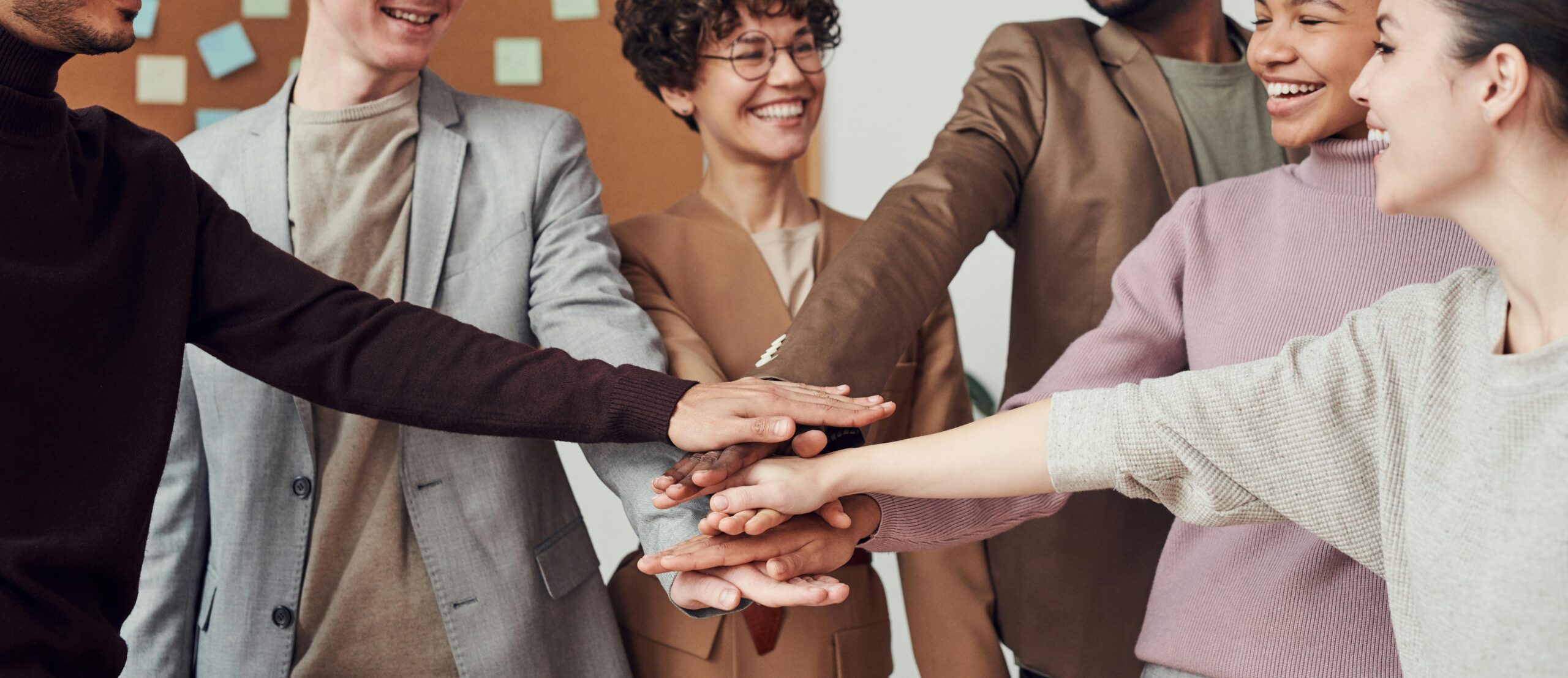 Diverse group of coworkers joining hands in unity, symbolizing teamwork, inclusion, and the importance of diversity in modern workplaces.