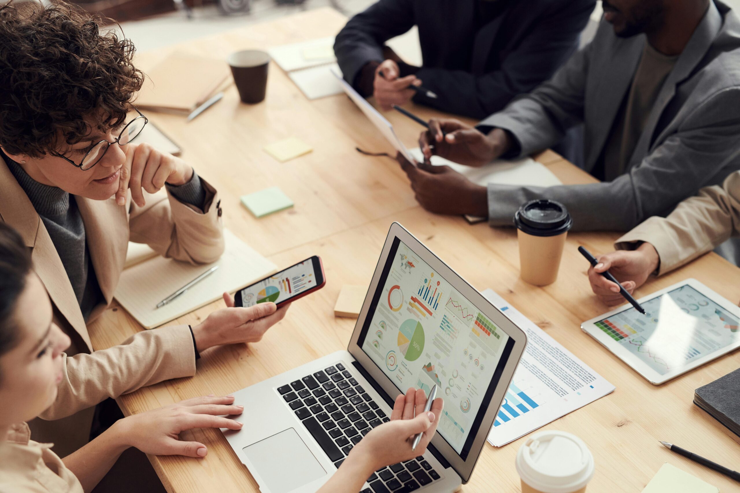 Business team reviewing charts and graphs on laptops, tablets, and documents during a meeting, illustrating data analysis and discussion on reducing HR risks for small businesses in Australia.