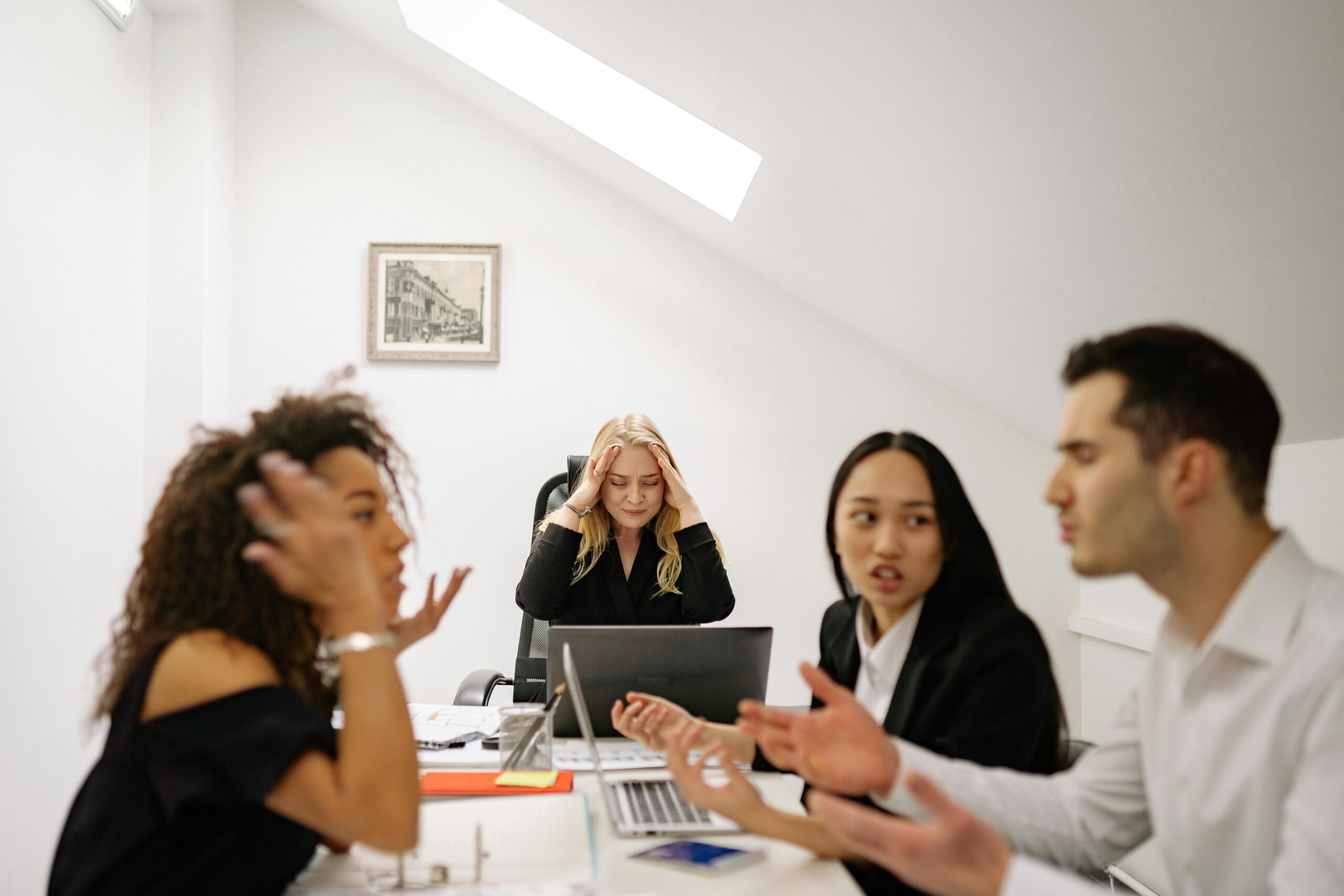 Frustrated business team in a workplace mediation session, with colleagues arguing while a stressed manager holds her head, illustrating challenges when conflict resolution fails.